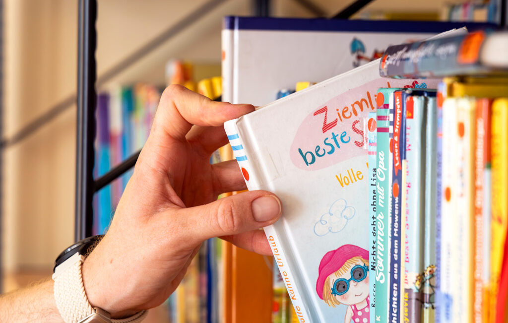 Eine Hand greift ein Kinderbuch in einem Regal.